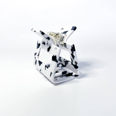 This is a miniature claw clip with a dalmatian print design, featuring irregular black spots on a white background. It has a classic spring-loaded hinge mechanism. The clip's compact size suggests it's ideal for securing smaller sections of hair, half-up styles, or for finer hair types.